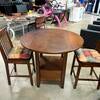 Round wooden high-top table with two wooden chairs and seat cushions.